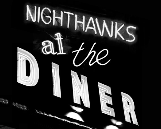 A black and white photo of a pub neon sign that says: Nighthawks at the Diner.