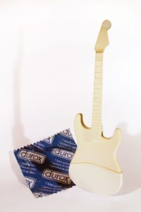a small shaped electric guitar painted in white and beige next to a Durex condom