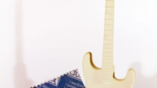 a small shaped electric guitar painted in white and beige next to a Durex condom