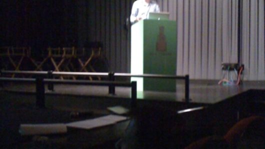 a man giving a speech form a green stand