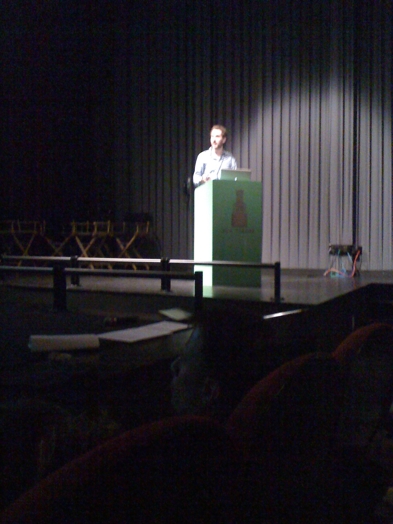 a man giving a speech form a green stand