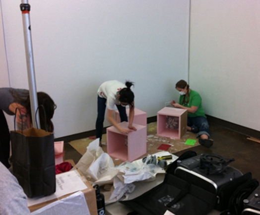 three people working on assembling pink boxes