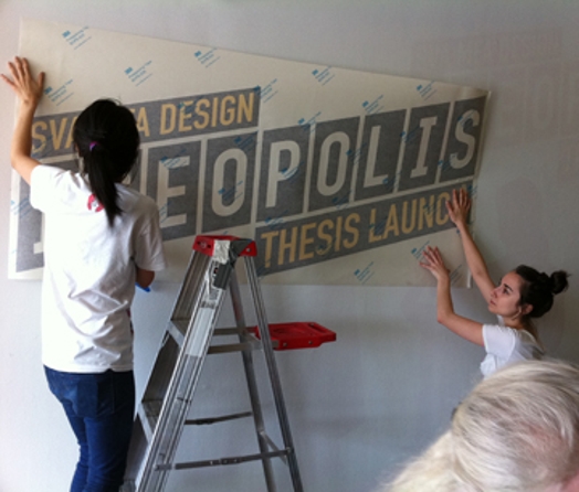 two girls installing the Ideopolis vinyl sicker on the wall