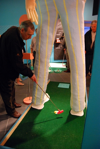 a man putting a golf ball in the hole of a mini-golf course with a man statue whit the ball whole between the statue's legs