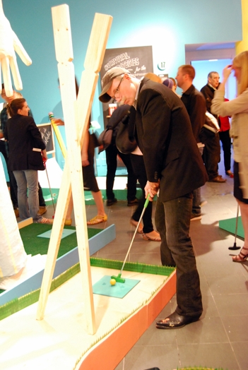 An older man is holding a golf cross to hit a small ball on a mini-golf course.