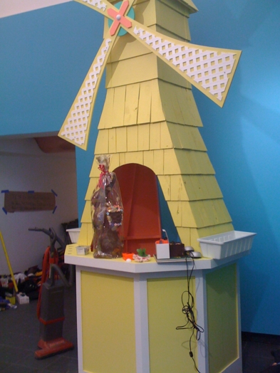 a yellow windmill sculpture with miscellaneous objects on it