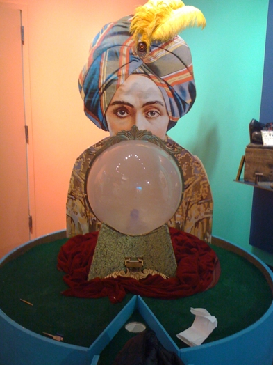 installation view of a sculpture with a head of an Arabic man with colorful clothes and in front of him is a crystal ball
