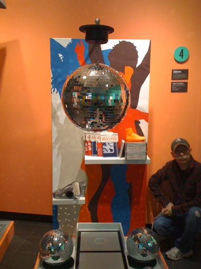installation view of a disco ball and a man sitting on the lower right corner