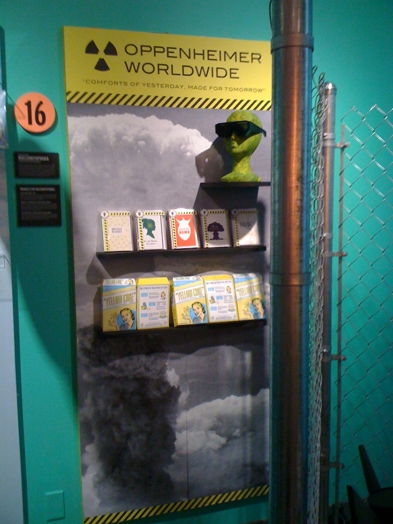 a wall with a shelf with flyers, booklets, and a small green head sculpture with sunglasses