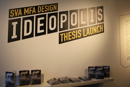 Ideopolis exhibition vinyl sticker applied on a wall and under it is a shelf with booklets about thesis exhibition