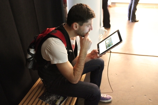 a man sitting on a bench is looking interested at an iPad's screen