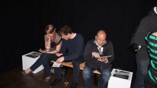 photo of three people sitting on a bench and looking on iPads