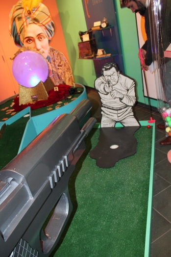 installation of a cardboard figure of a man pointing a and in his shadow is the whole for the mini-golf ball