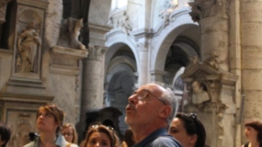 A photo of a group of people visiting a cathedral and its arches sculpted in stone.