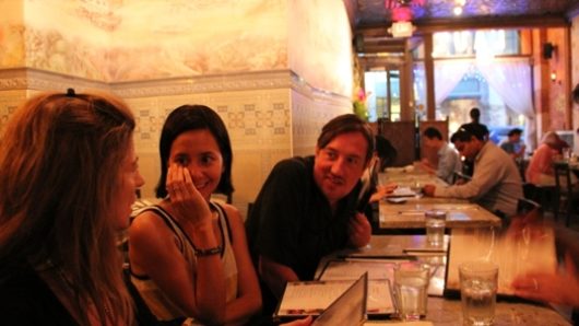 three people are talking while they are sitting at a table in a dim-lit room