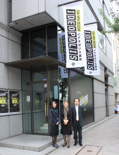 portrait of two women and a man in front of the IDEOPOLIS banner on the sidewalk in front of the building