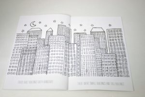 an opened coloring book with tall buildings and a starry night sky with the moon on the left side