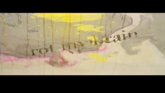 a still from a clip with abstract paint stains and the words "rot my brain" visible on a turbid water surface