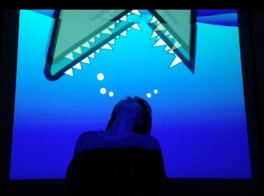 a still from a movie with a person at the bottom of the frame, in a mostly blue environment, and from the top of the frame comes down an illustration of a fish month with sharp teeth