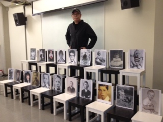 a man standing behind two rows of chairs with portraits on them