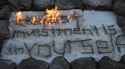 an arrangement surrounded with stones and the words formed with sticks: the best investment is in yourself; the wording is set on fire
