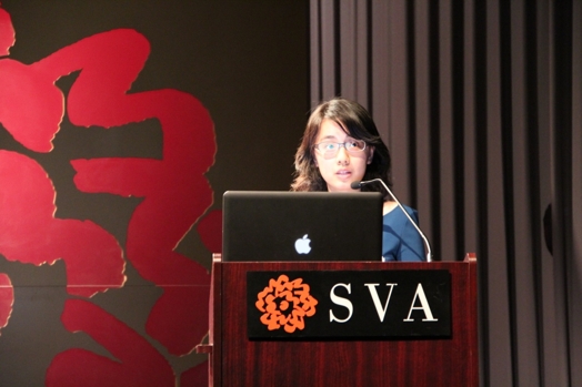 a woman giving a speech from a stand in the "designer as" thesis presentation