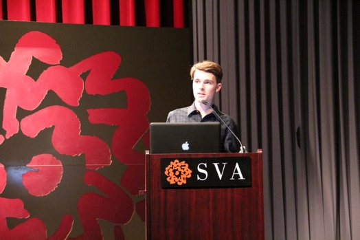 a man giving a speech from a stand in the "designer as" thesis presentation