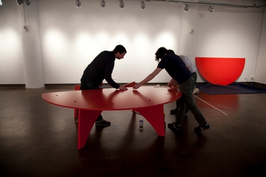 people installing a red rounded table in the designer as exhibition gallery