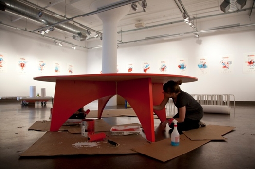 a woman working on a red rounded table in the exhibition gallery
