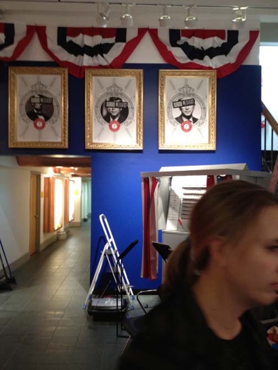 Three headshot portraits hung on the wall with three faces covered with a black stripe with text.