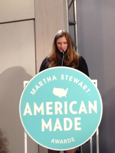 a woman giving a speech on the stand with the Martha Stewart American Made awards logo