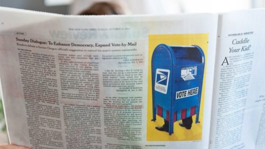 A photo of a newspaper with a picture of a blue mailbox with feet on it.