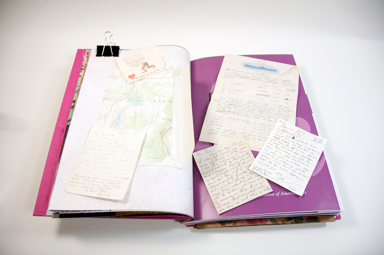 an opened book depicting fragments of handwritten pages of notebooks on the left and right page, and on the left page is also a part of a map