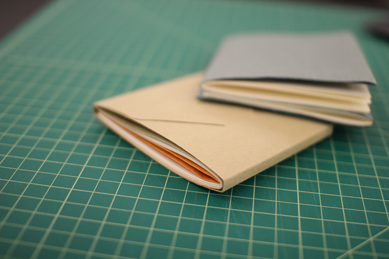 two notebooks covered with light brown and grey covers were placed on a green measuring table