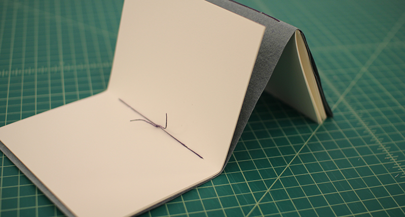a notebook cover made from a light brown material tied up with the purple thread on the middle section