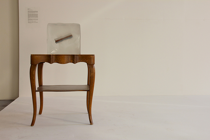 A wooden chair with a transparent acrylic cube with a book in it.