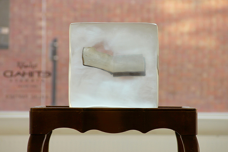 A wooden chair with a transparent acrylic cube with a book in it.
