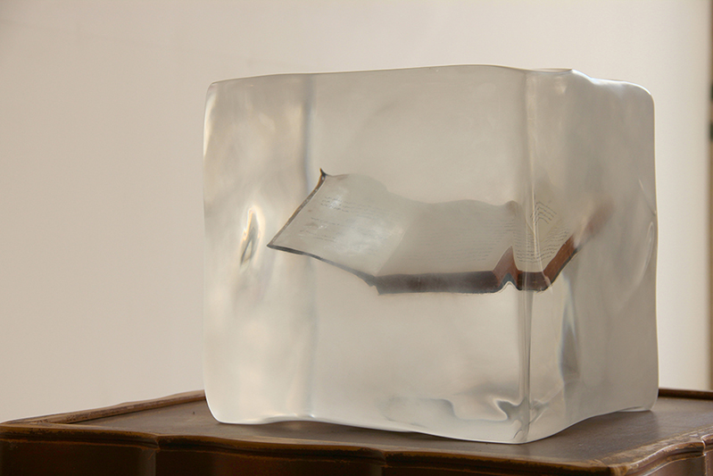 A wooden chair with a transparent acrylic cube with a book in it.