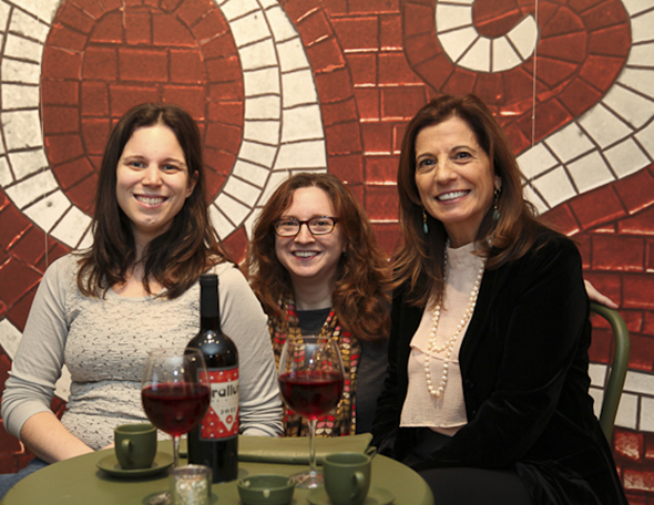three women sitting at a table, each having a glass of wine
