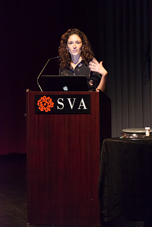 Portrait of a woman giving a speech from a wooden stand with the SVA logo on it