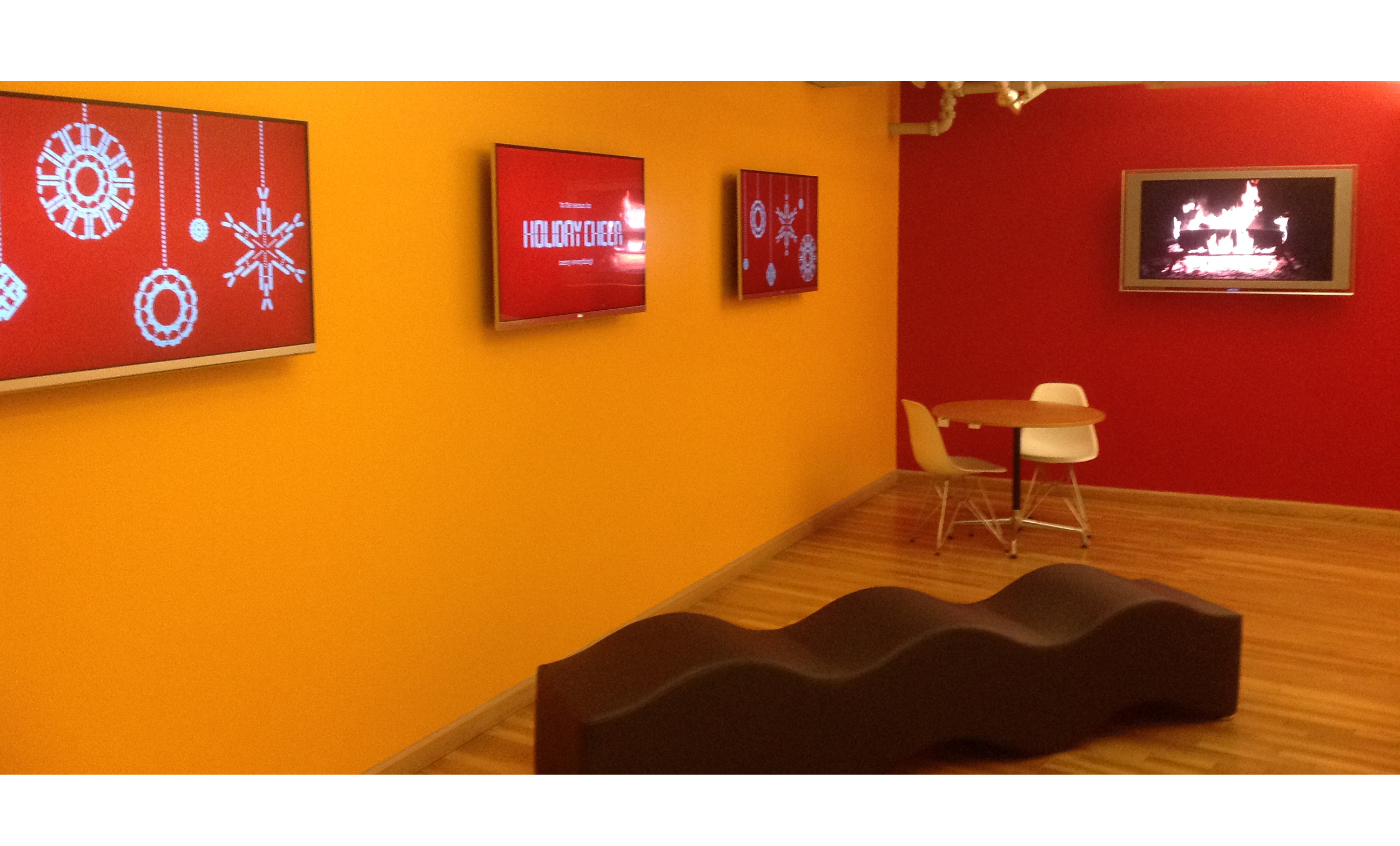 exhibition gallery with yellow wall and tv's with red images on them