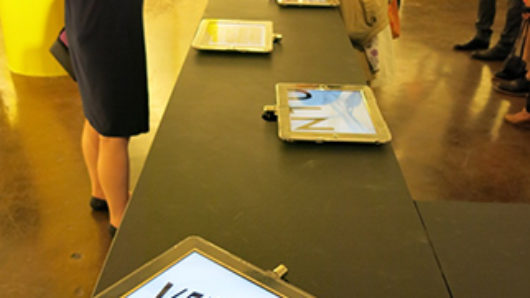 venture logo on an iPad screen sitting on a table and two persons in the back of the frame