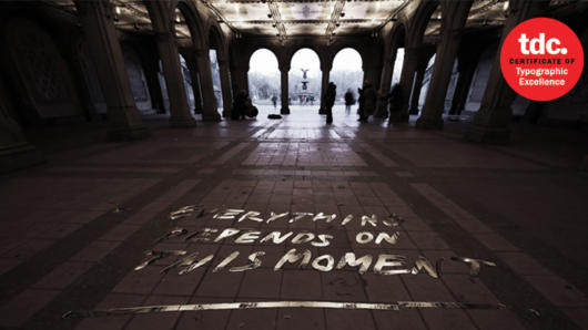 A poster showing the entrence to a building and some peoples walking. On th poster there is a 3D text: Everything depends on this moment.