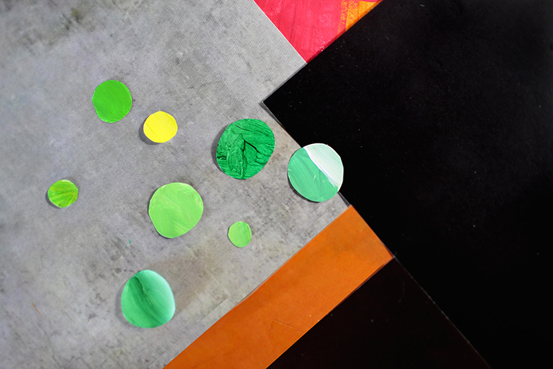 A set of grey, brown, black and red pieces of paper and over them some green lime and yellow colored circles made also from paper.