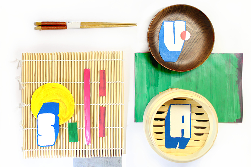 A set of eating wooden sticks, some wood plates, a bamboo table pad and some colorful papers. There are also the letters SVA on each item.