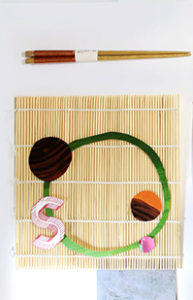 A srt of eating sticks near a bamboo table pad with some colored paper on it.
