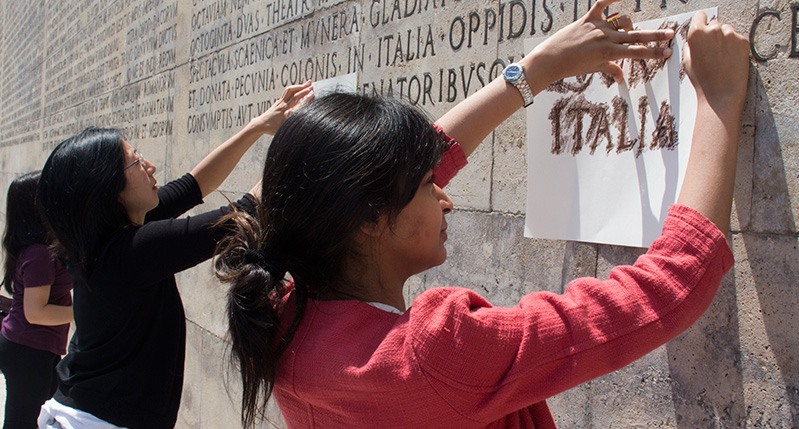 people making frottage on letters on roman wall