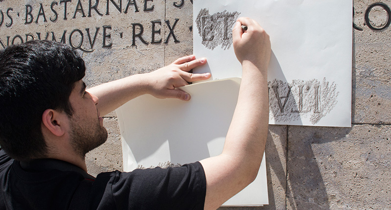 man making frottage on letters on roman wall