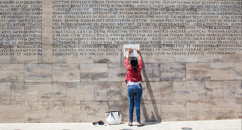 woman making frottage on letters on roman wall