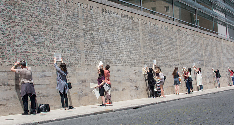 people making frottage on letters on roman wall